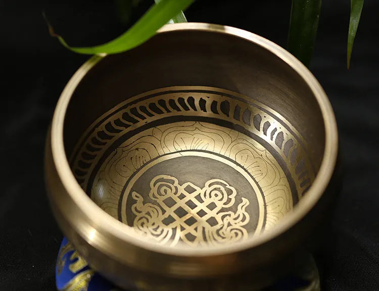 Handmade copper singing bowl with auspicious knot design on a soft surface with leather stick