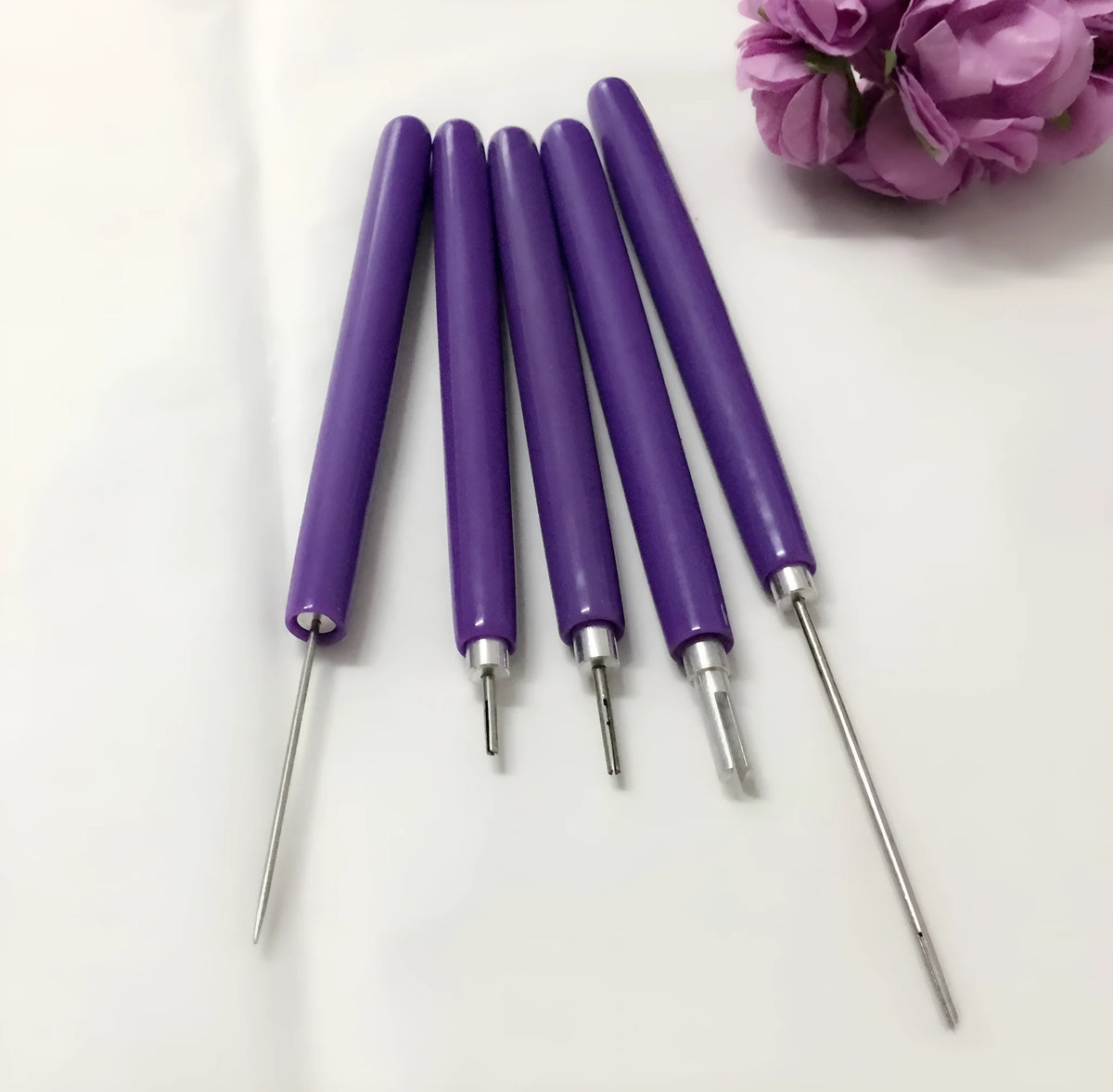 Purple quilling paper tool set with five slotted pens and needle stylus on white background