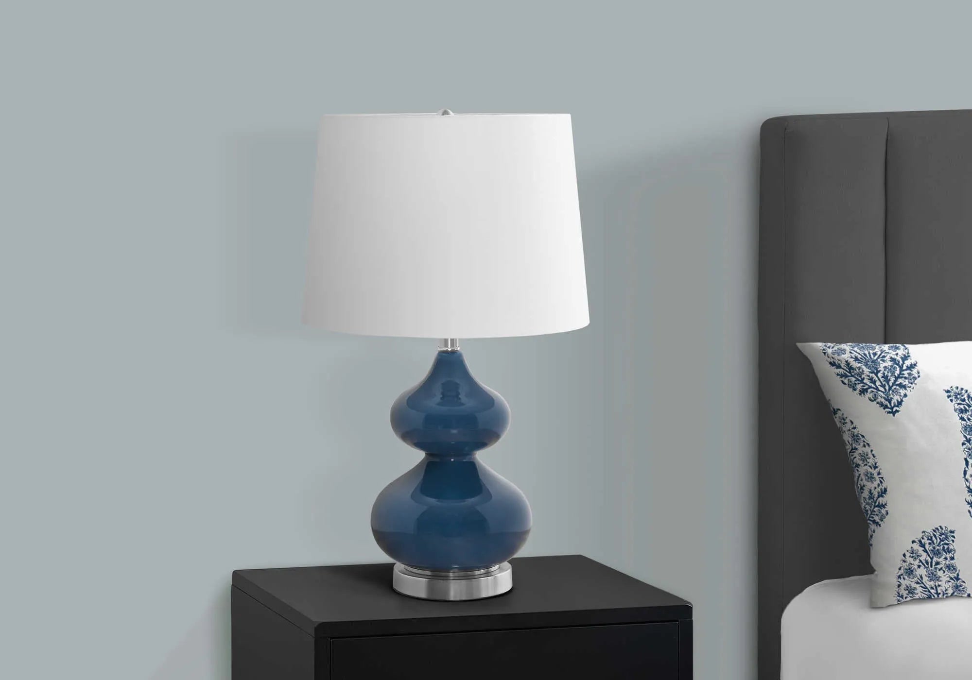 Blue cloth shade desk lamp with a clear crystal glass base on a wooden desk.