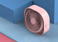 Pink USB rechargeable desk fan with rotating head on a wooden desk.