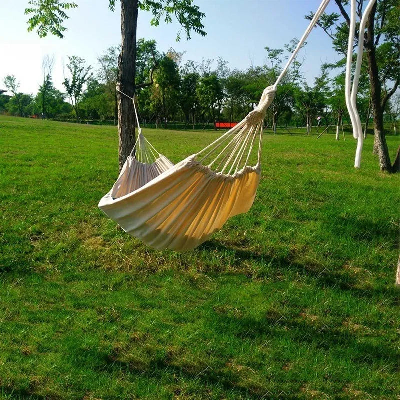 Cotton camping hammock with strap and bandage set up between trees for outdoor use