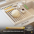 Milky White foldable stainless steel kitchen draining rack shown beside a sink, demonstrating its tri-fold mechanism.