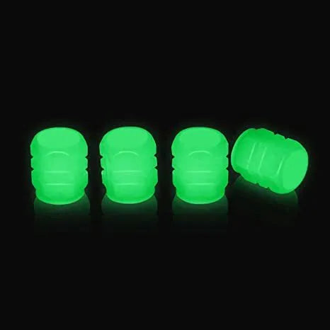 Set of four glowing green LED tyre valve caps screwed onto a car wheel valve stems at night.