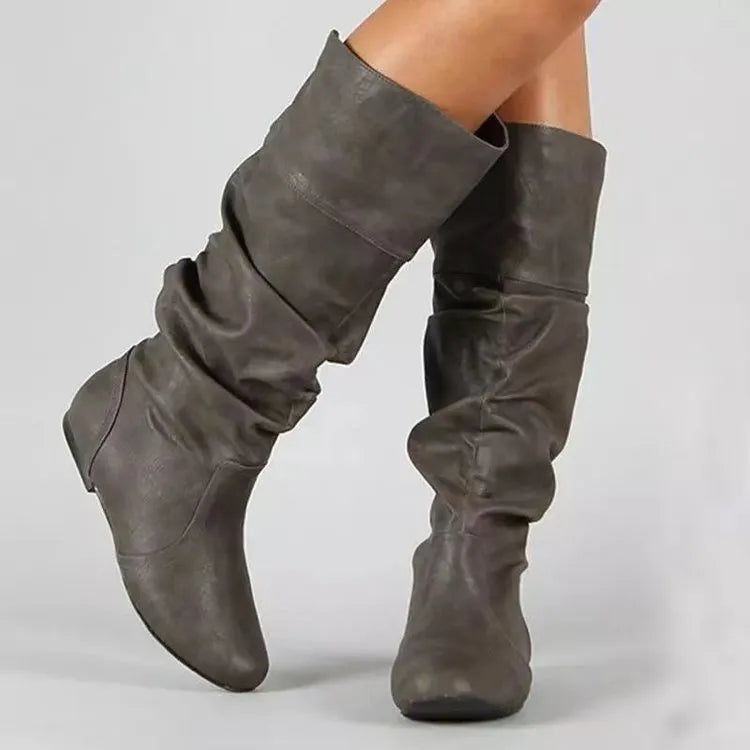 Women's flat black slip-on boots with a round toe and high cylinder shaft on a neutral background.