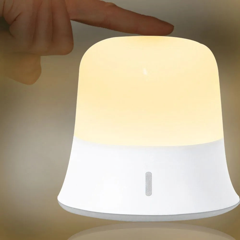 White touch control bedside night light with rechargeable battery and motion sensor on a table.