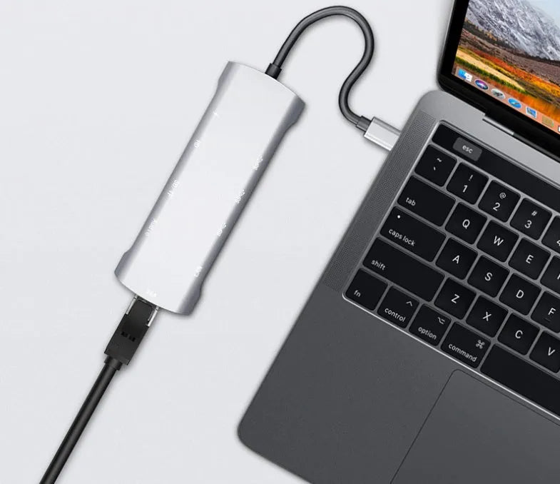 Grey aluminium USBC docking station with HDMI, VGA, USB 3.0, and charging ports on a desk.