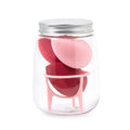 Three cosmetic sponges in different shapes placed on a holder next to a clear jar containing additional sponges.