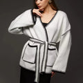 Loose beige knitted cardigan with a lace-up front, worn open over a white top.