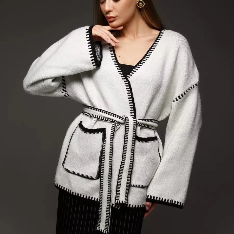 Loose beige knitted cardigan with a lace-up front, worn open over a white top.