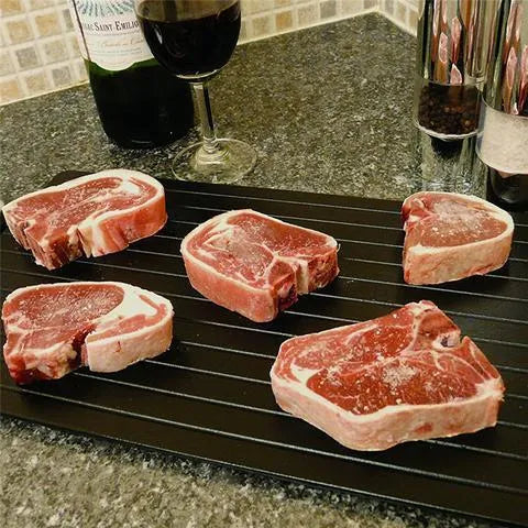 Black aluminium fast defrosting tray with silica gel feet on a kitchen countertop.