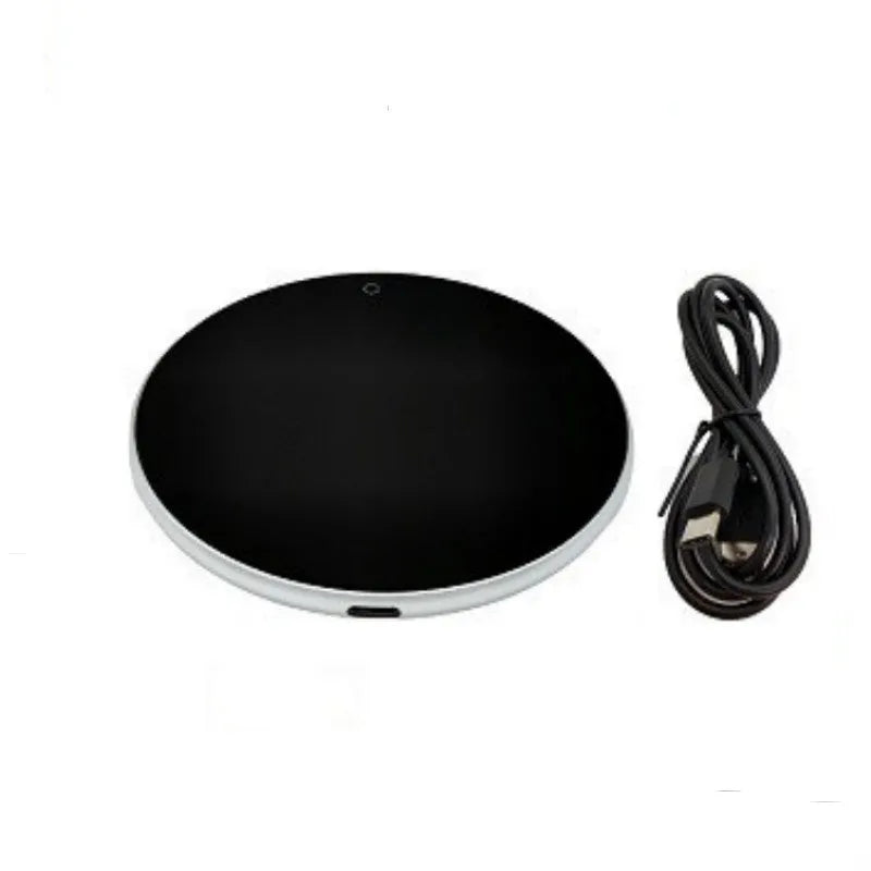 Black USB heating coaster with tempered glass plate on a desk next to a coffee mug