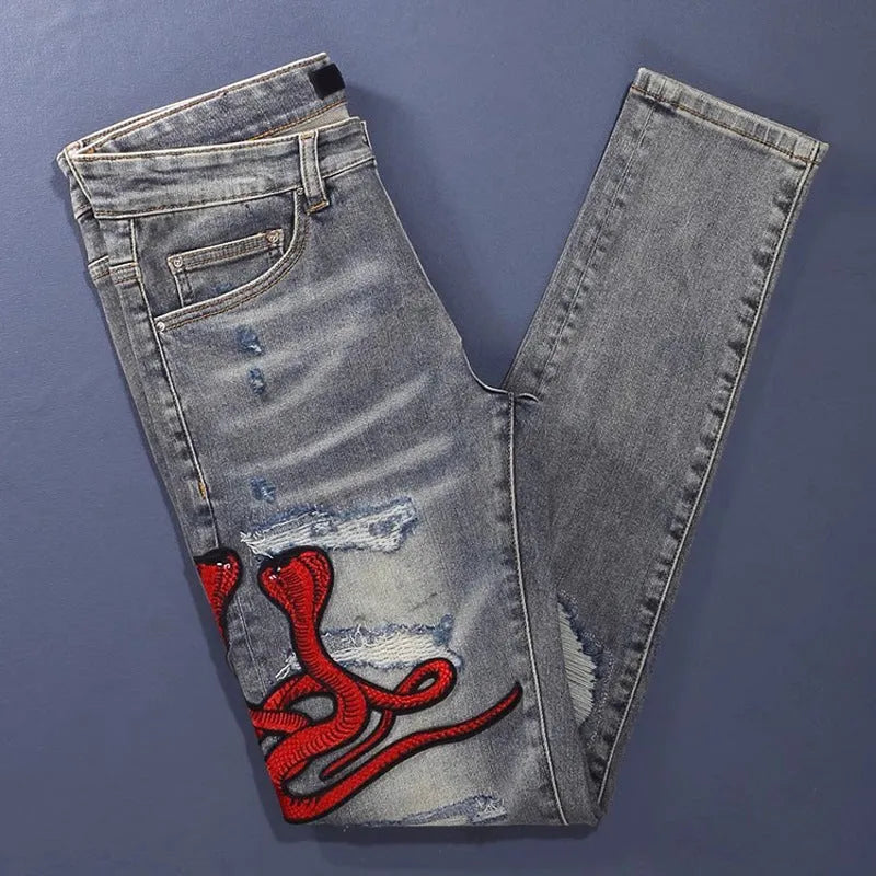 Man wearing slim-fit light blue jeans with distressed knee patches and embroidered back pocket detail.