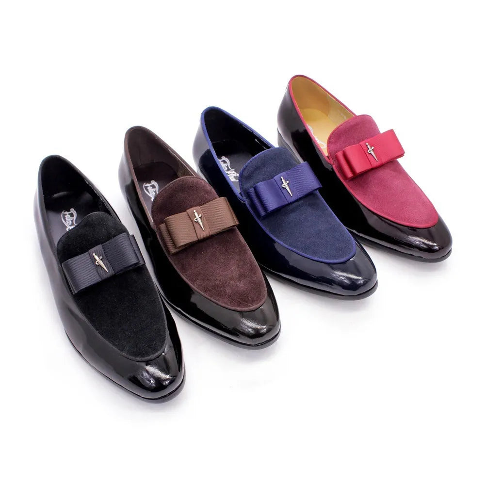 Men's glossy black patent leather tassel loafers with a low-top design and rubber sole on a wooden floor.