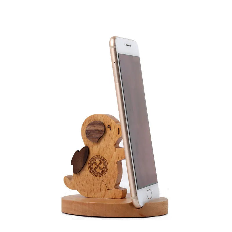 Solid beech wood phone stand with a decorative resin puppy figurine, holding a mobile phone at an angle with a charging cable threaded through the back.