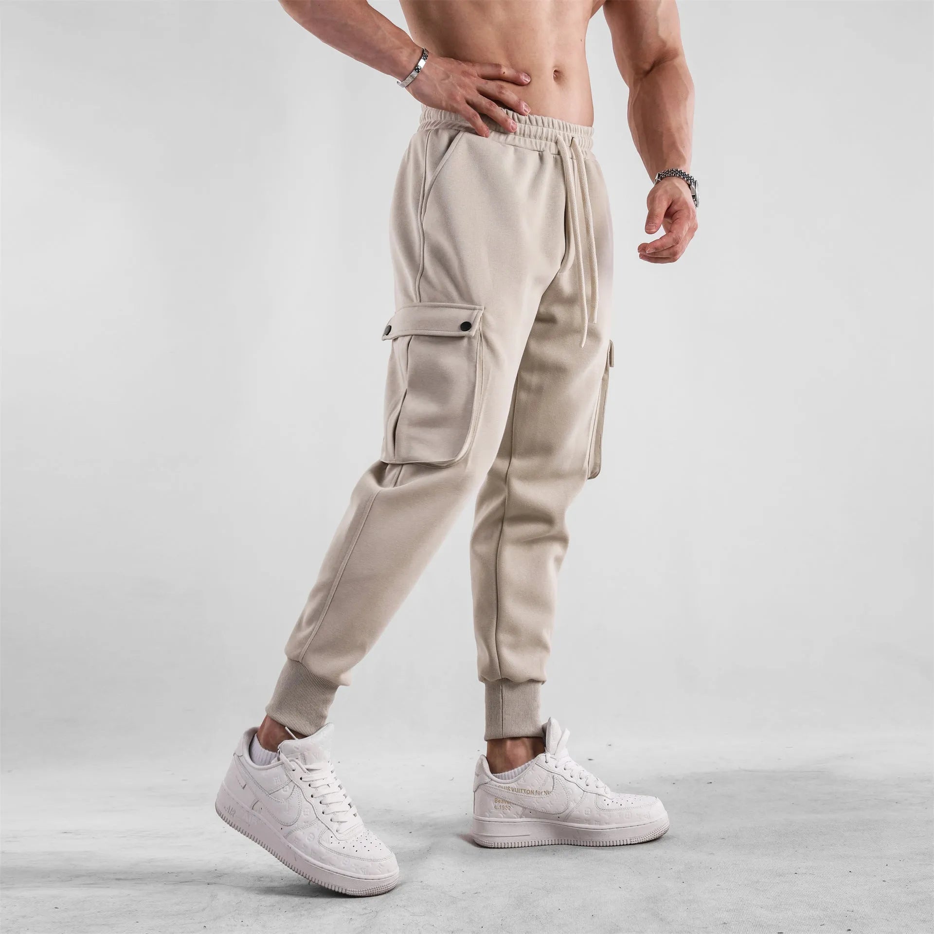 Men's loose-fit beige trousers with ankle ties and multiple pockets, laid flat.