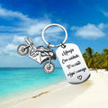 Stainless steel motorcycle-themed key ring with inspirational design on a flannel storage bag.