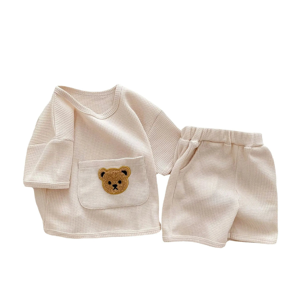 Unisex baby summer suit with bear print cotton top and beige shorts on a neutral background