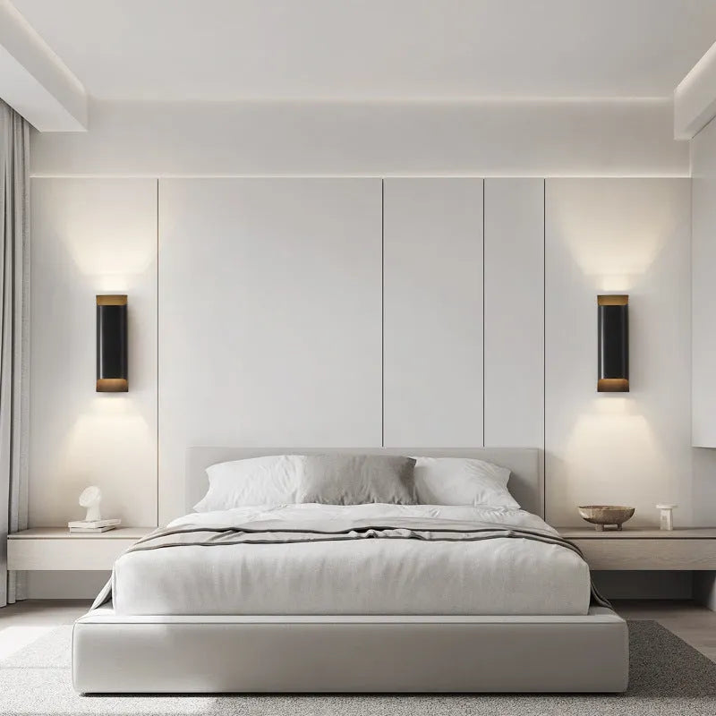 Minimalist copper wall lamp in black gold finish mounted beside a bed.