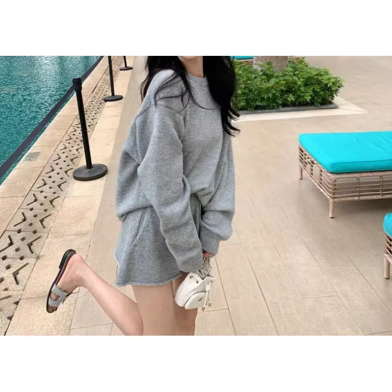 Woman wearing a loose beige knitted sweater and matching wide-leg shorts, a loungewear set on a neutral background.