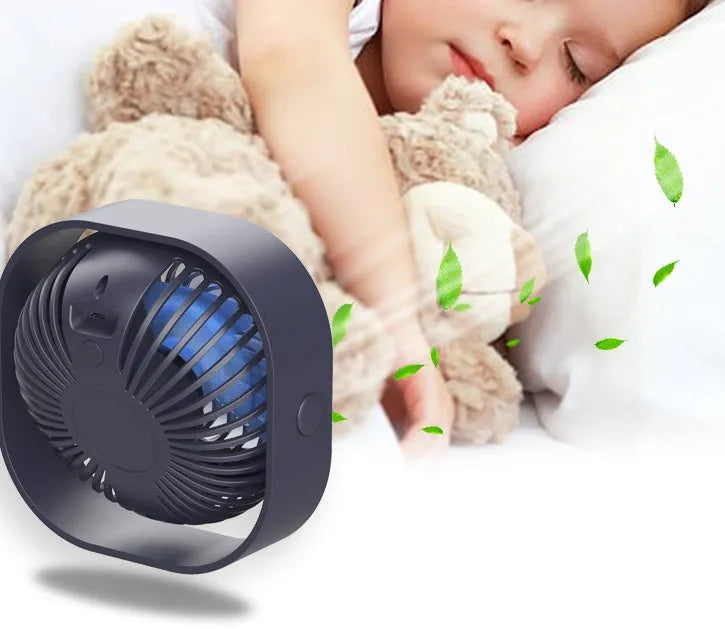 Pink USB rechargeable desk fan with rotating head on a wooden desk.