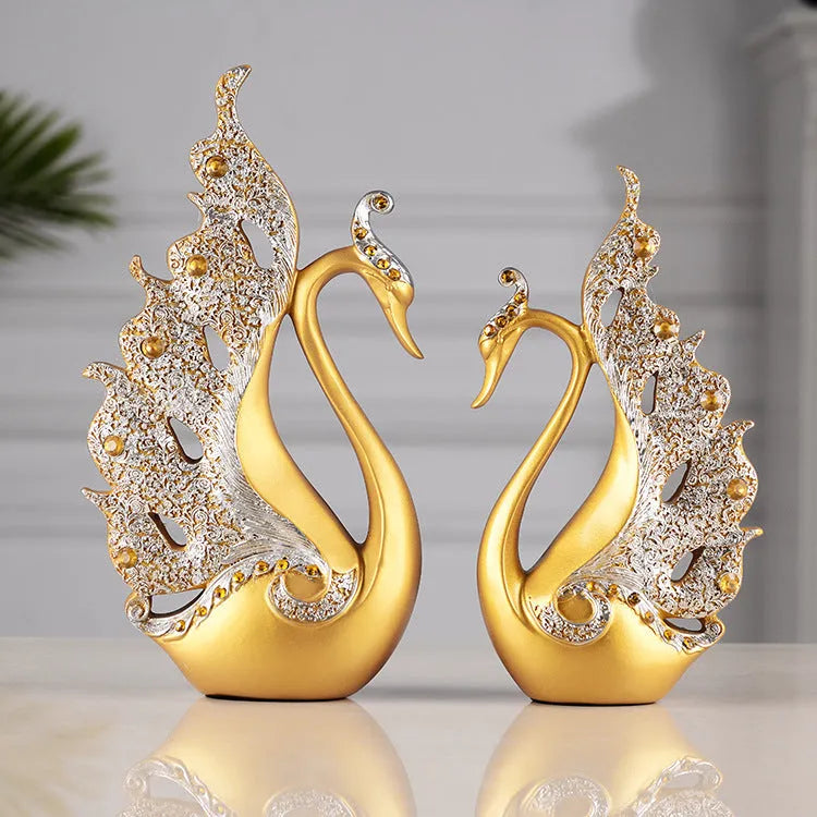 Resin couple swan figurines in blue and gold, large 29cm and small 24cm, on a wooden table