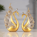 Resin couple swan figurines in blue and gold, large 29cm and small 24cm, on a wooden table