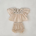 Apricot cotton two-piece suit with floral pattern, square collar top, and wooden horn buttons, next to matching bloomer pants.