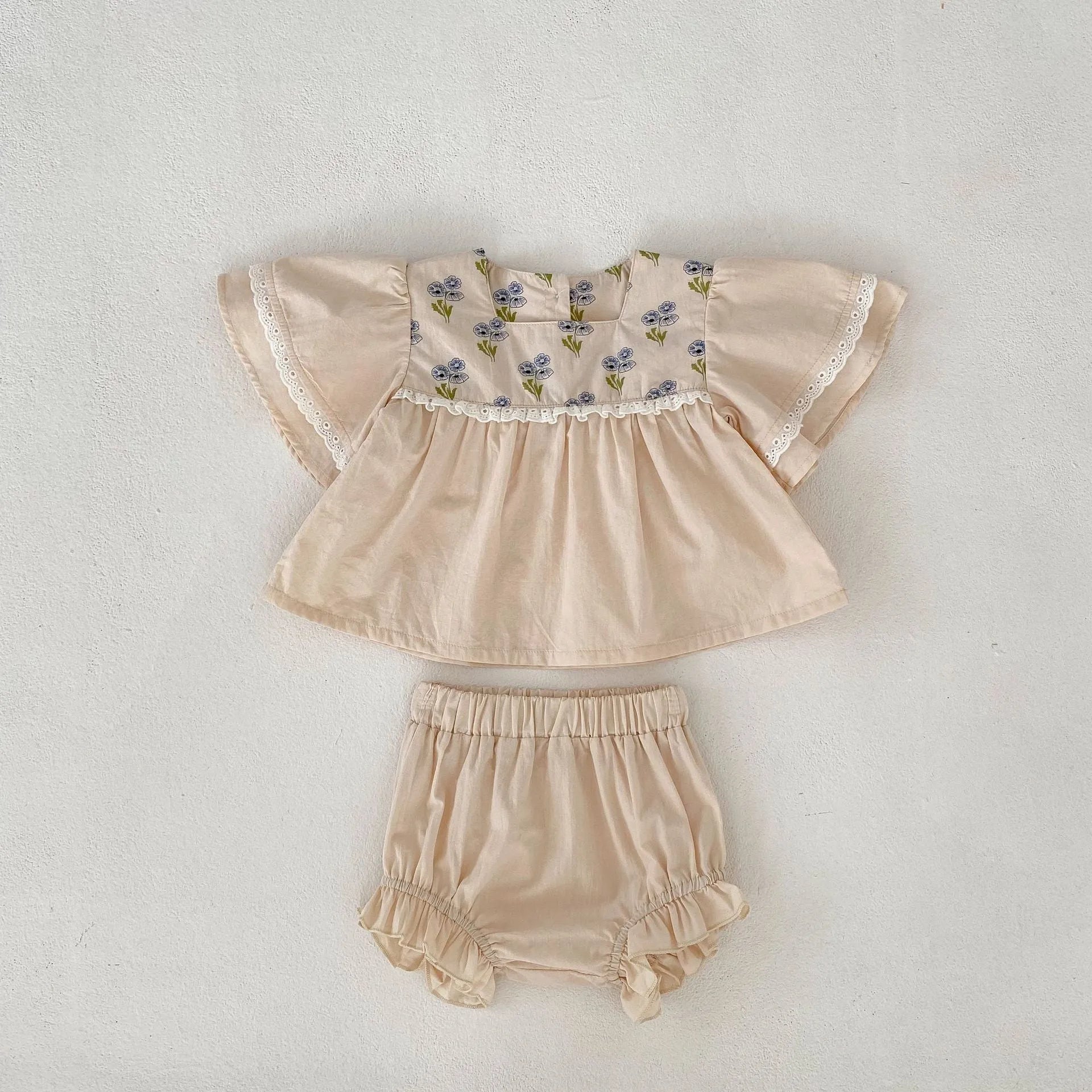 Apricot cotton two-piece suit with floral pattern, square collar top, and wooden horn buttons, next to matching bloomer pants.