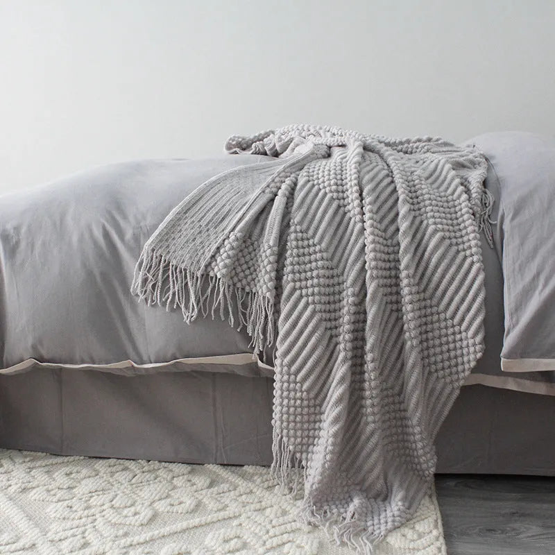 Small grey polyester nap blanket measuring 127 by 170 centimetres folded on a sofa.
