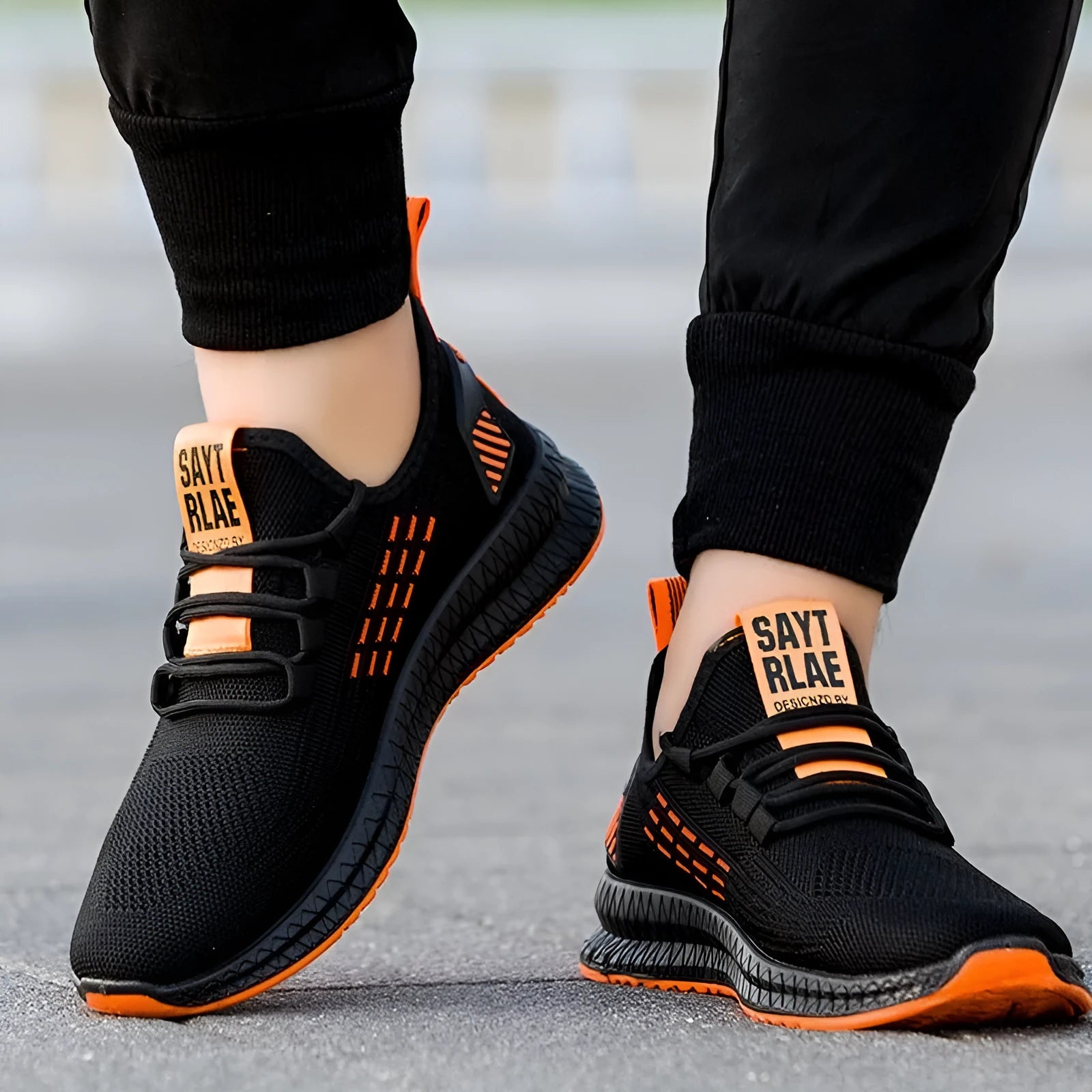Men's low-top black casual trainers with cross-strap detail and flying weave upper, shown on a white background.