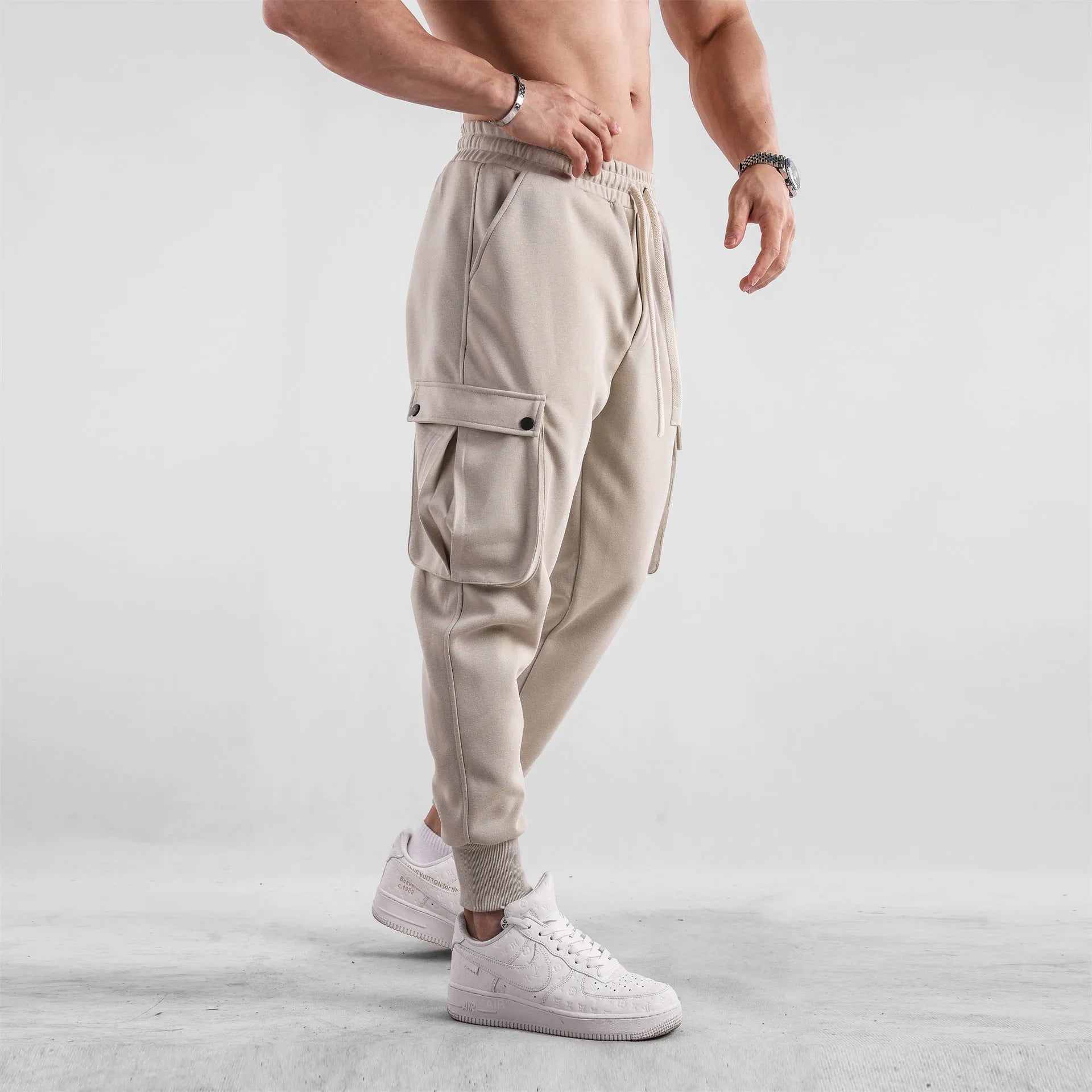 Men's loose-fit beige trousers with ankle ties and multiple pockets, laid flat.