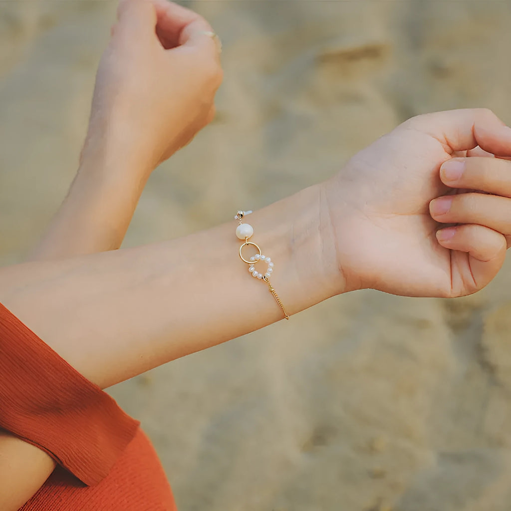 Women's natural freshwater pearl bracelet with gold-plated clasp and floral charm accents on a white background.