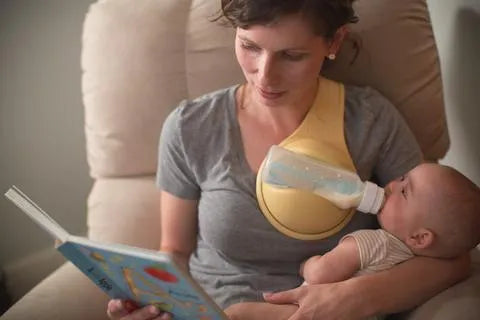 Yellow plastic hands-free baby bottle holder on a white surface, showing the bottle slot and ergonomic curve, 48x16x13cm