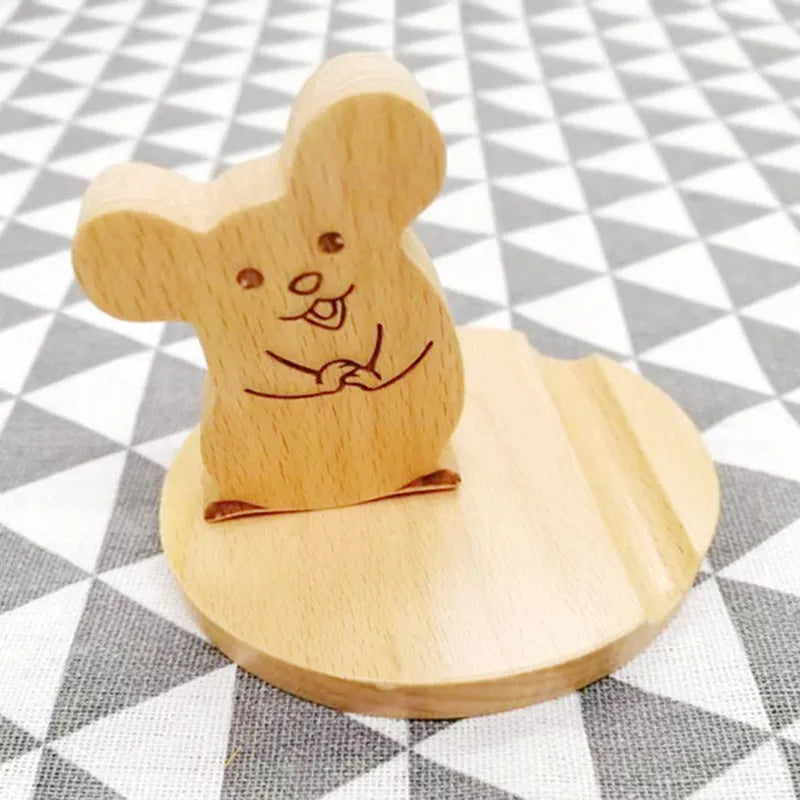 Solid beech wood phone stand with a decorative resin puppy figurine, holding a mobile phone at an angle with a charging cable threaded through the back.
