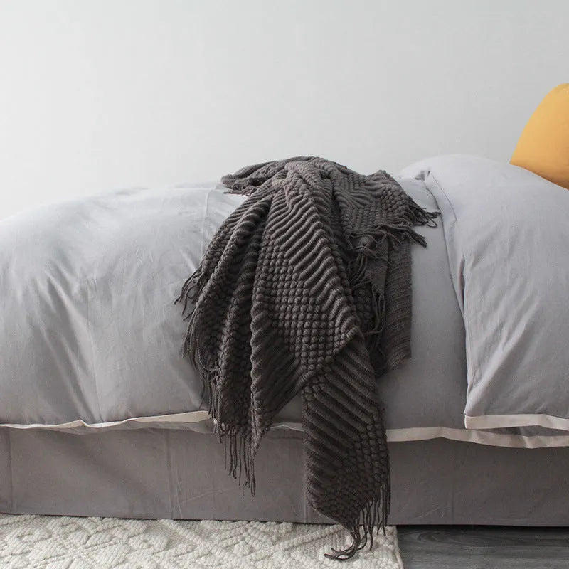 Small grey polyester nap blanket measuring 127 by 170 centimetres folded on a sofa.