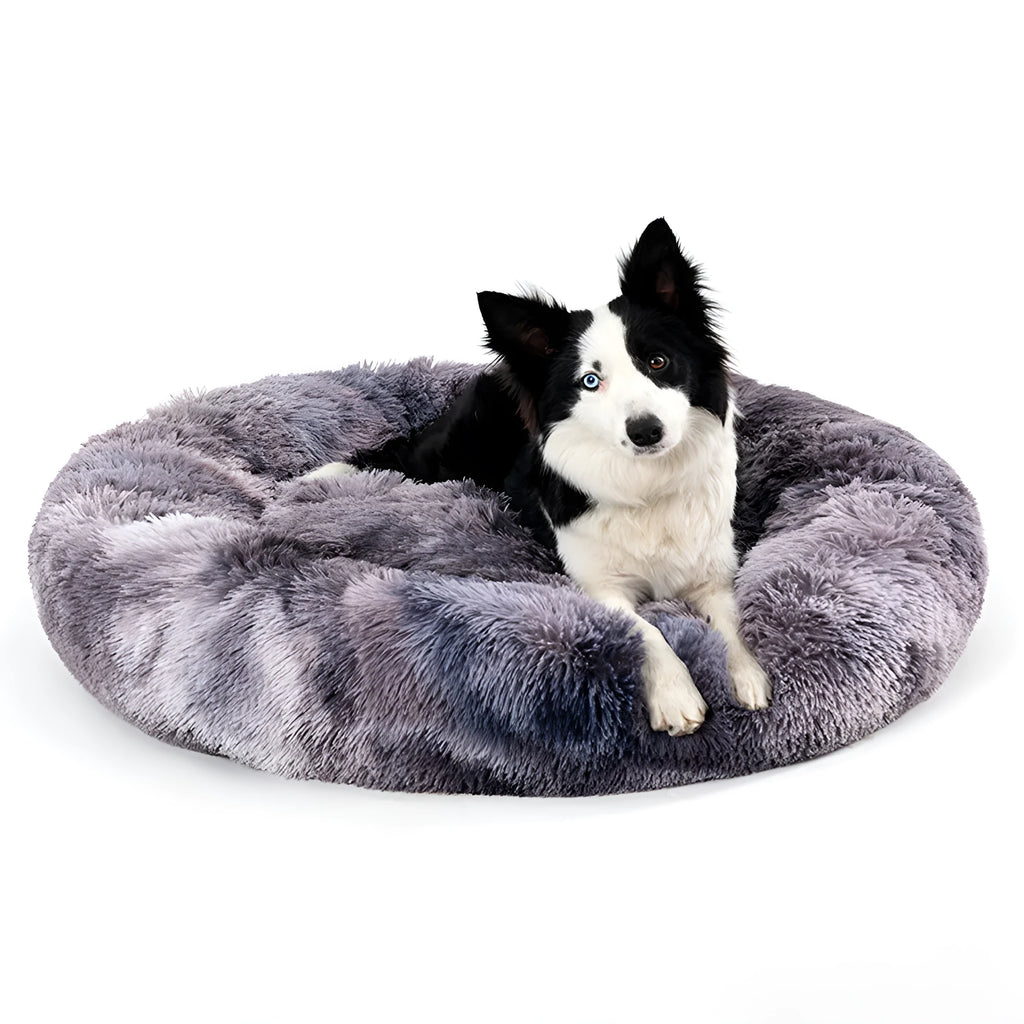 Fluffy donut-shaped pet bed in long plush fabric, shown in a light grey colour with a raised edge.