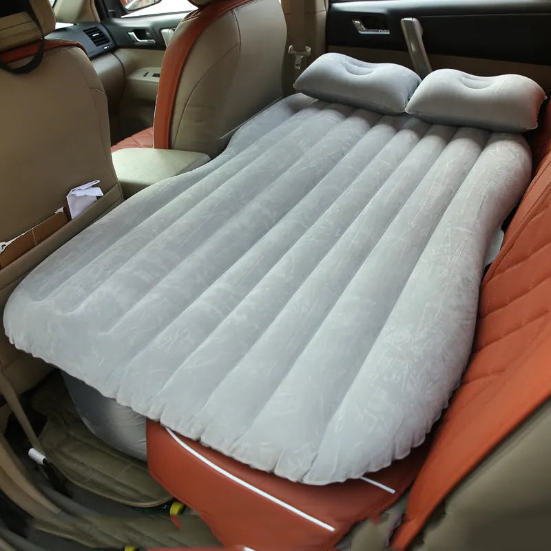 Inflatable car bed with flocking material shown in vehicle with two pillows and storage bag