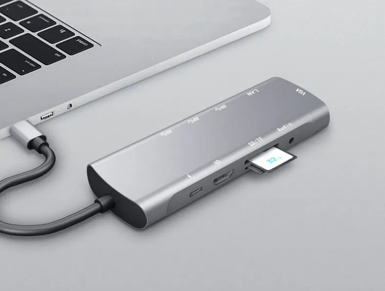 Grey aluminium USBC docking station with HDMI, VGA, USB 3.0, and charging ports on a desk.
