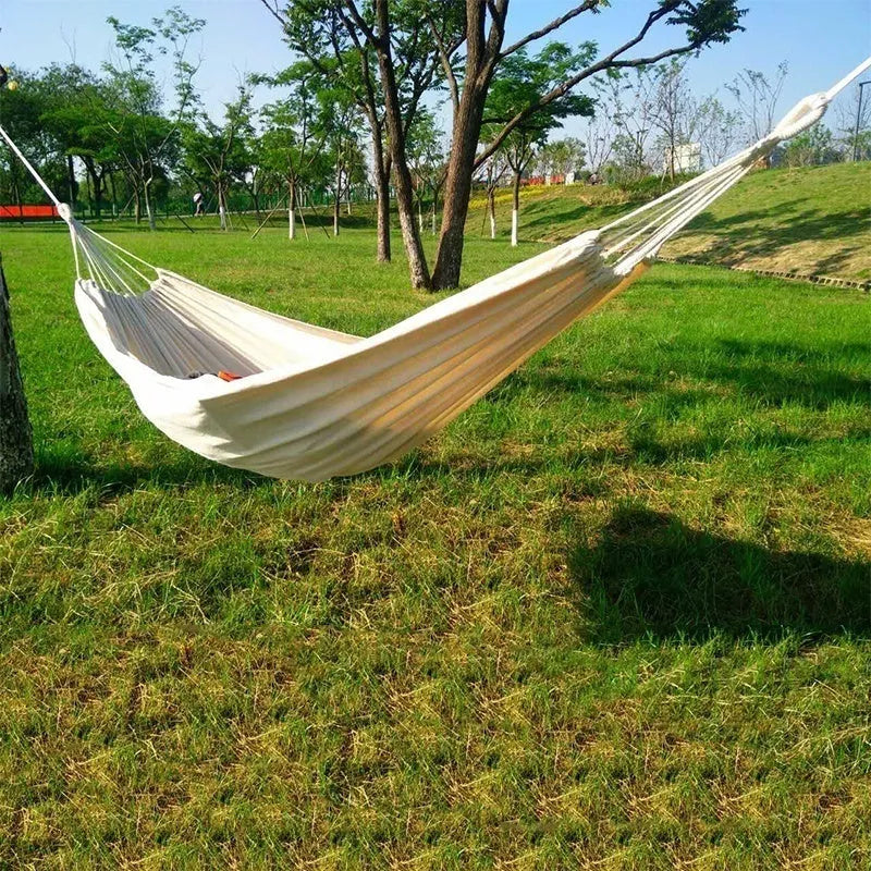 Cotton camping hammock with strap and bandage set up between trees for outdoor use