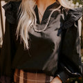 Black women's long-sleeve blouse with a V-neck, ruffle trim, and contrast stitching.