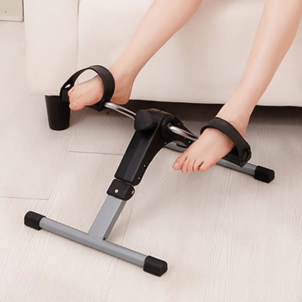 Silver and black exercise mini spinning bike on hard floor with pedals and non-slip foot pads