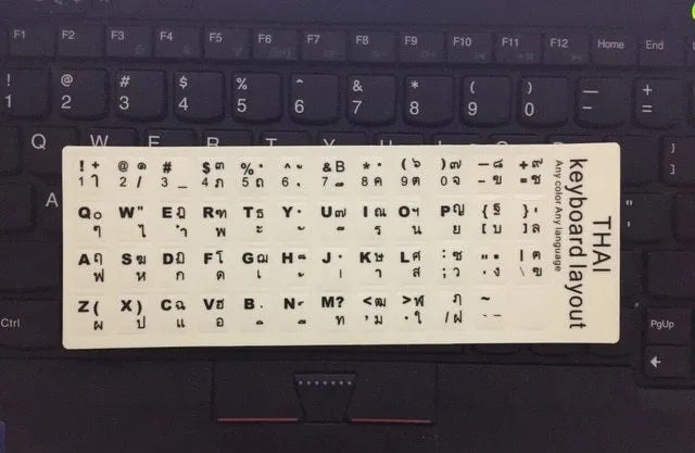Glowing yellow multilingual keyboard stickers showing Arabic, Thai, Hebrew, French, Italian and German characters