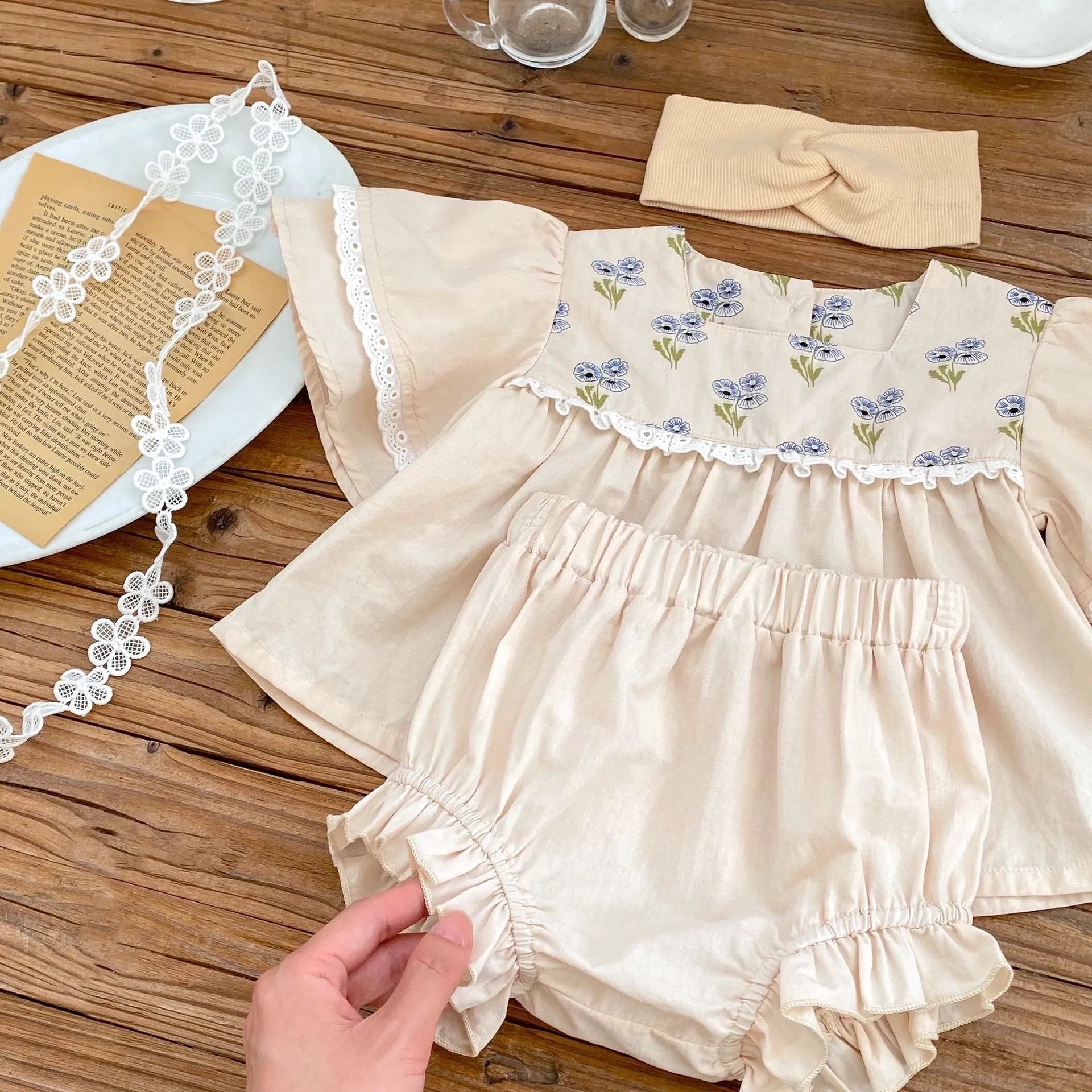 Apricot cotton two-piece suit with floral pattern, square collar top, and wooden horn buttons, next to matching bloomer pants.