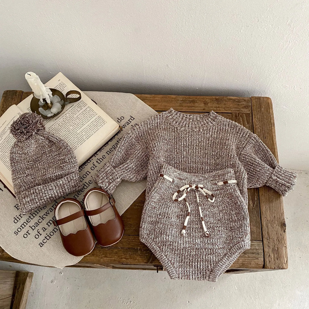 Dark brown knitted three-piece set for infant girl with fur ball hat, blouse, and shorts.