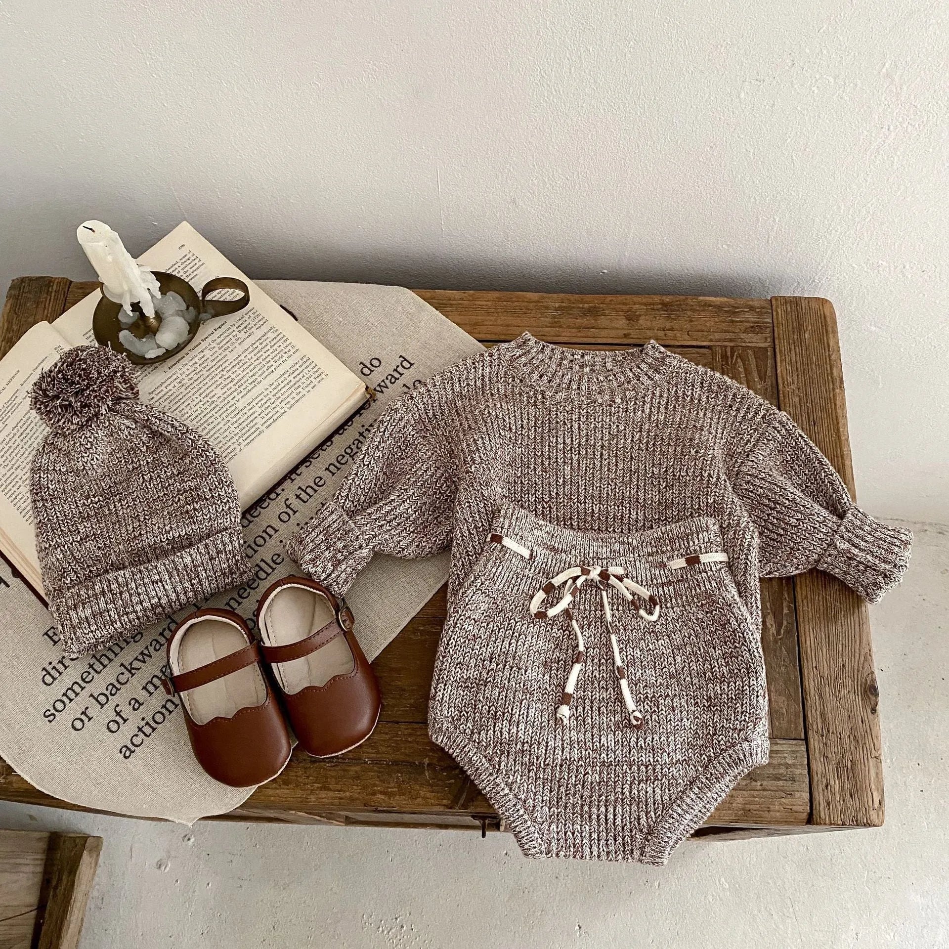 Dark brown knitted three-piece set for infant girl with fur ball hat, blouse, and shorts.