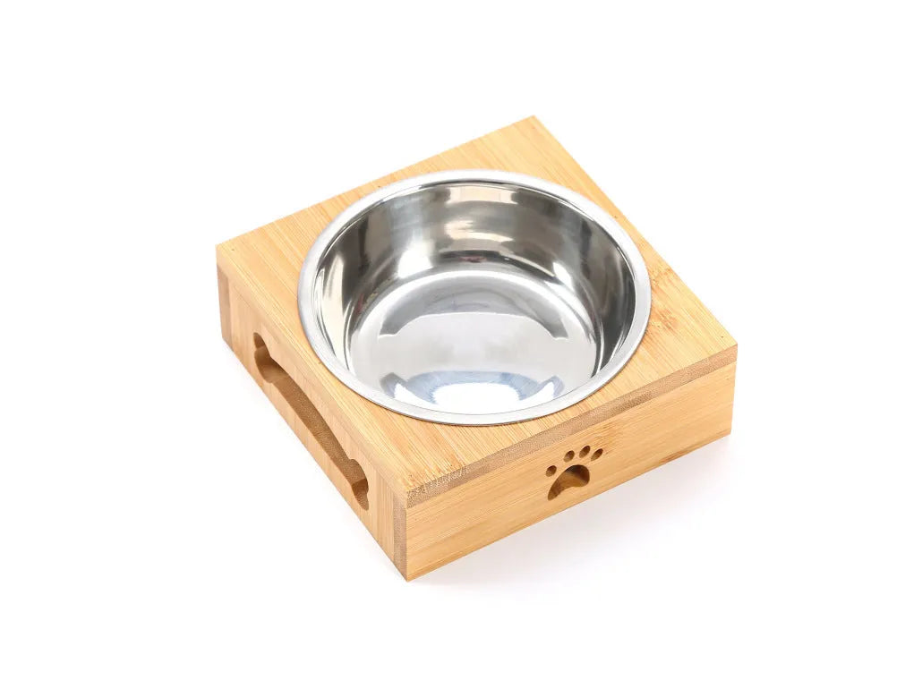 Solid wood elevated pet feeder with stainless steel bowls in a bamboo finish on a wooden floor.