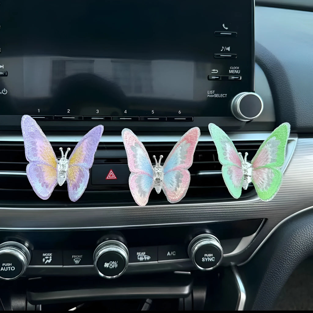 Soft fabric embroidered butterfly car air vent decoration in multiple colour options on a centre console.