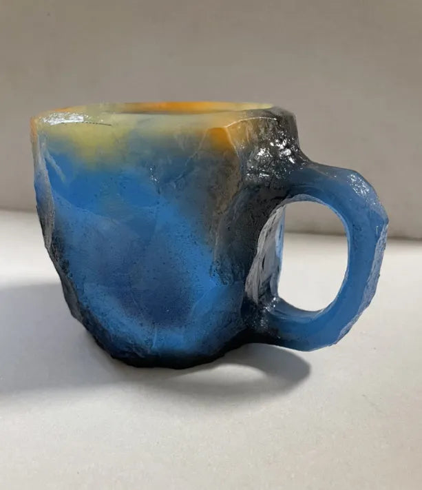 A purple resin coffee mug with a handle, showing a crystal-like structure, on a table.
