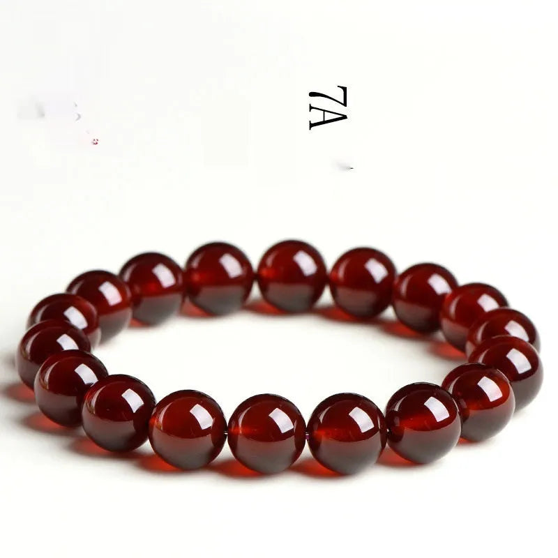 Close-up of a natural orange red garnet bead bracelet with a metal Ruyi charm on a wrist.