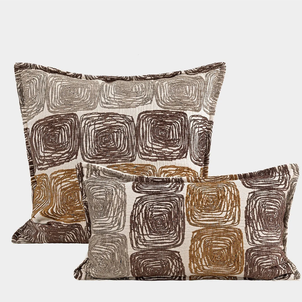 Cream and coffee coloured abstract coil pattern square and waist pillow covers on a sofa.